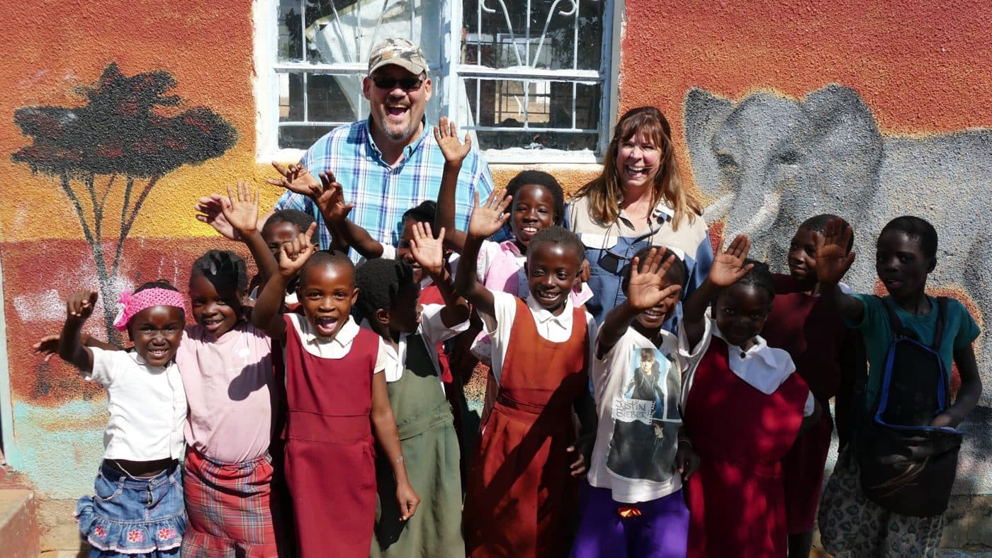 Dr. Johnson and Lisa smiling and waving with a group of schoolchildren