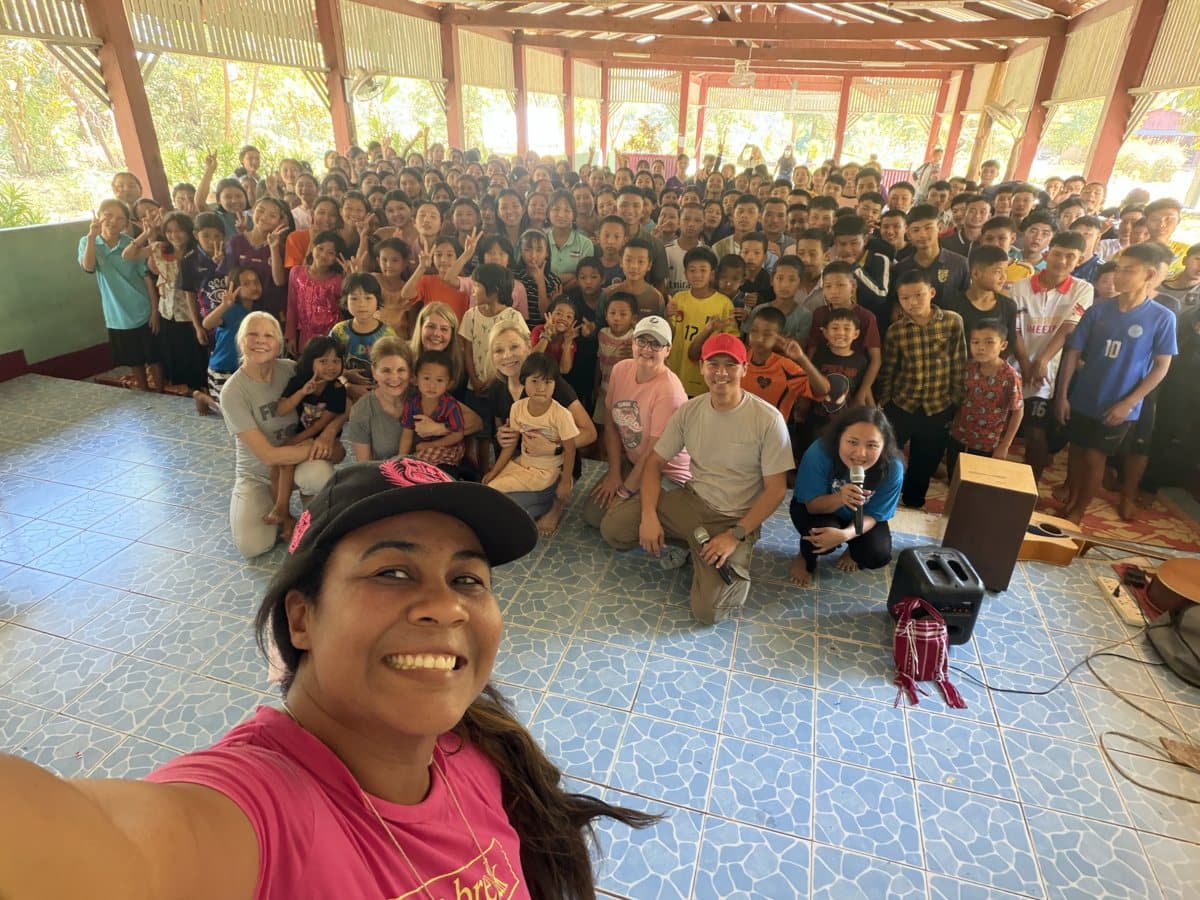 Em taking a selfie with a large group of smiling children and volunteers