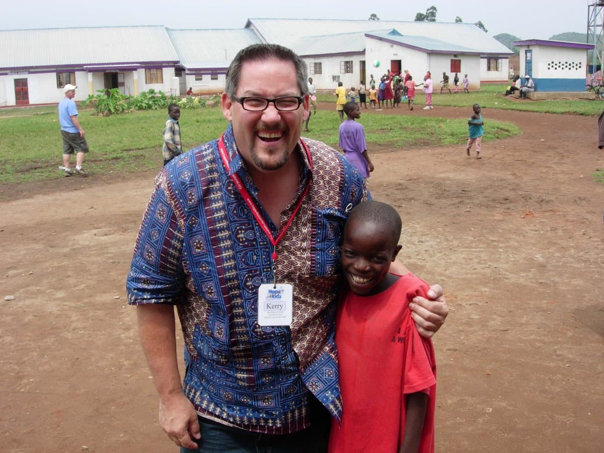 Dr. Johnson laughing with his arm around a boy at a school in Uganda